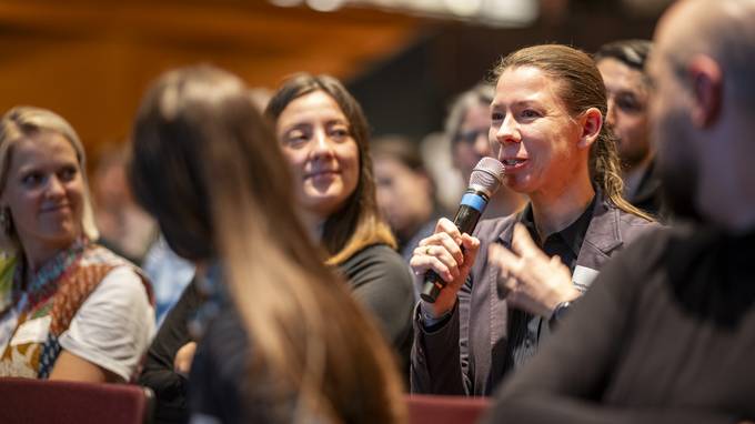 Besucher bei einer Konferenz, eine Frau im Publikum spricht ins Mikrofon (öffnet Vergrößerung des Bildes)