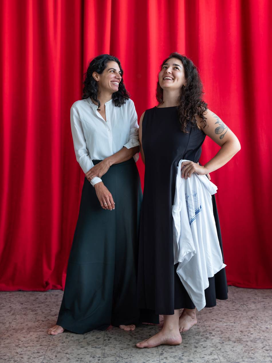 Two dark-haired, smiling, self-confident women in front of a red velvet curtain