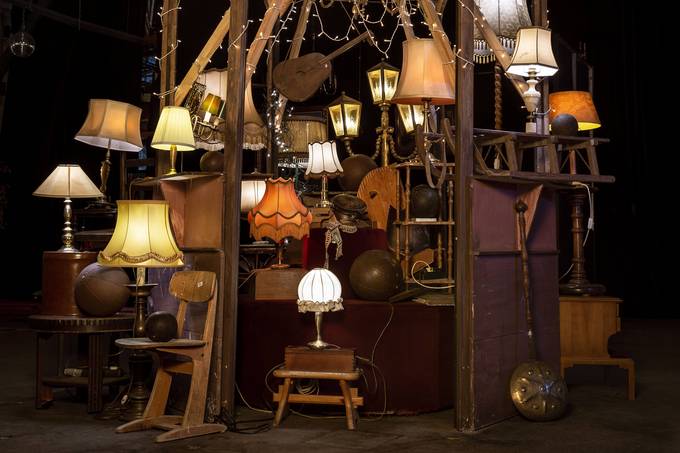 Foto von einer großen Zahl in der Bildmitte gestapelter antiker Lampen, dazwischen auch alter Stühle und andere Möbel in dunklem Holz